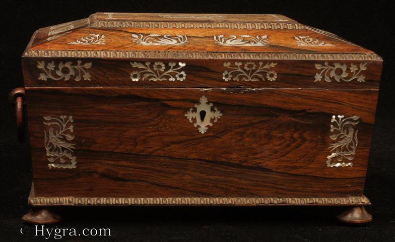 -Antique box in the sarcophagus form. The box is veneered in figured rosewood and is inlaid in mother of pearl depicting stylized flora with birds. The fluid design of stylised flora is exceptionally fine. This is a spectacular box which encapsulates the best of the Regency era. The box stands on turned rosewood feet and has turned rosewood drop ring handles. The centre panel of the top is framed with gadrooning as is the pediment adding the architectural impact. The box has a lift out tray which has been relined . Circa1825. Enlarge Picture